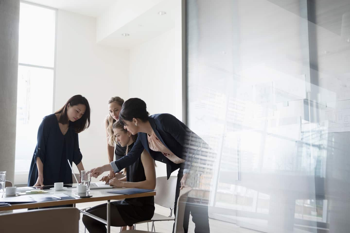 Four women in a meeting staring and pointing at a laptop screen.