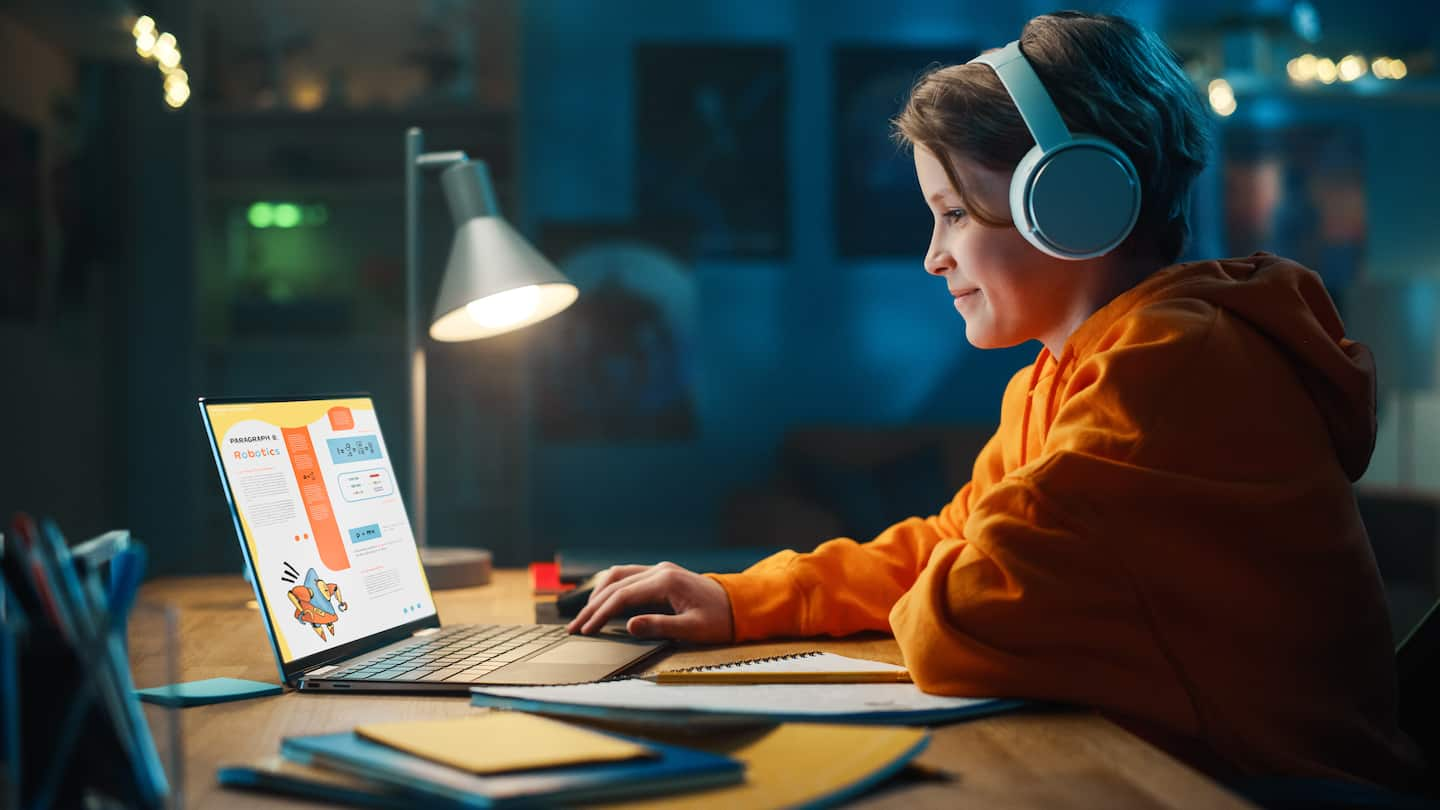 Smart student in headphones researching homework on a laptop computer., writing in a notebook, studying school material.