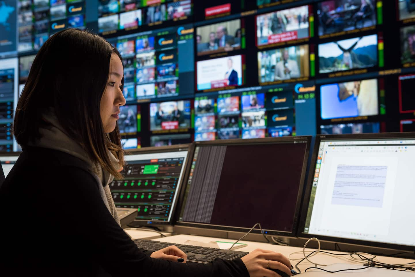 Woman at desk working on multiple computer monitors.