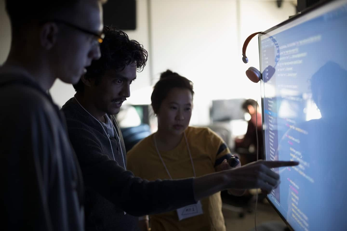 Three I.T. professionals looking at a computer monitor., with one person pointing to the screen.