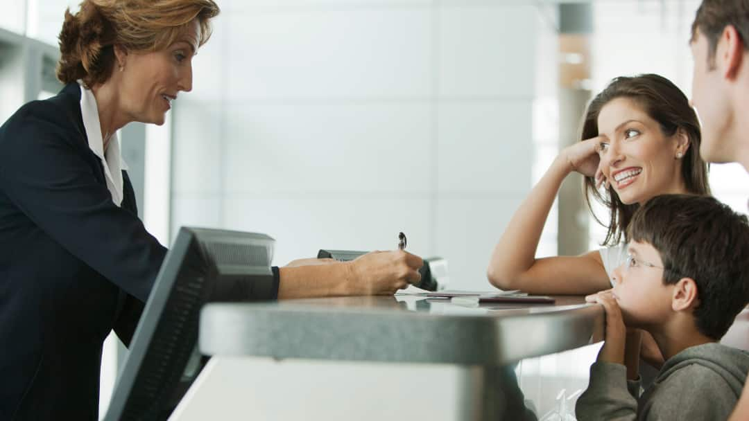 Photo of a hotel receptionist working at the front desk and checking guests into their hotel reservation.